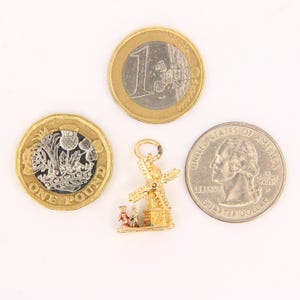 May include: Gold charm of a windmill with two figures standing in front of it. The charm is about the size of a US quarter.
