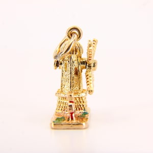 May include: A gold charm in the shape of a windmill with a red roof and green and yellow accents. The charm is detailed with a small windmill blade and a loop for attaching to a necklace or bracelet.