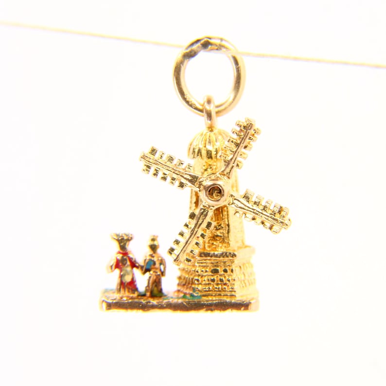May include: Gold charm of a windmill with two figures in front of it. The windmill is detailed with a gold roof and a red and blue painted base.