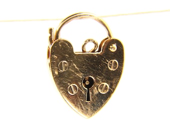 May include: A heart-shaped gold padlock with a keyhole and a curved handle. The padlock has visible screw heads and a key inserted on the side. The lock is suspended against a white background.