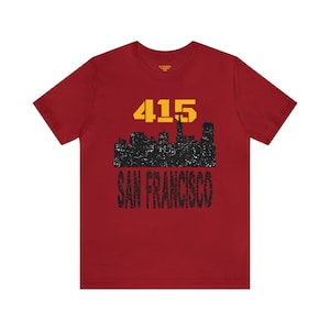 Puede incluir: Camiseta roja con un gráfico negro y amarillo del horizonte de San Francisco y el número 415.