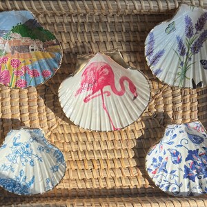 Puede incluir: Cinco conchas decorativas con ribete dorado, cada una con un patrón floral diferente. Las conchas están dispuestas sobre una superficie de mimbre tejido.