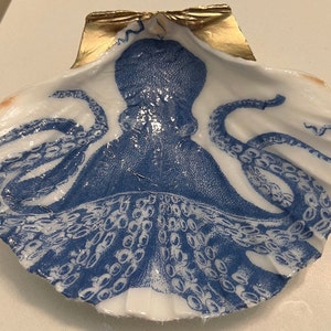 May include: A white seashell with a blue and white octopus design. The shell has a gold rim.