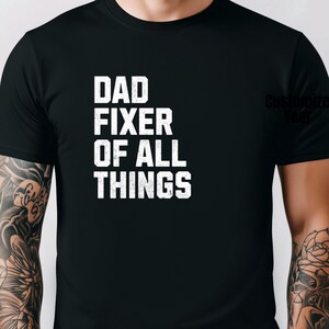 Könnte beinhalten: Schwarzes T-Shirt mit weißem Text, der "Dad Fixer of All Things" lautet.