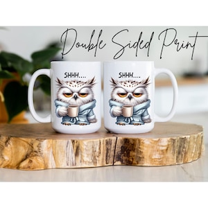 May include: Two white ceramic mugs with a double-sided print. Each mug features an illustration of an owl wearing a blue robe and holding a coffee cup. The text "SHHH...." is above the owl. The words "Double Sided Print" are written above the mugs.