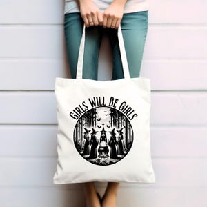May include: White tote bag with black text and graphic. The text reads "Girls Will Be Girls". The graphic is a circle with a moon, bats, and five witches standing around a cauldron in a forest.