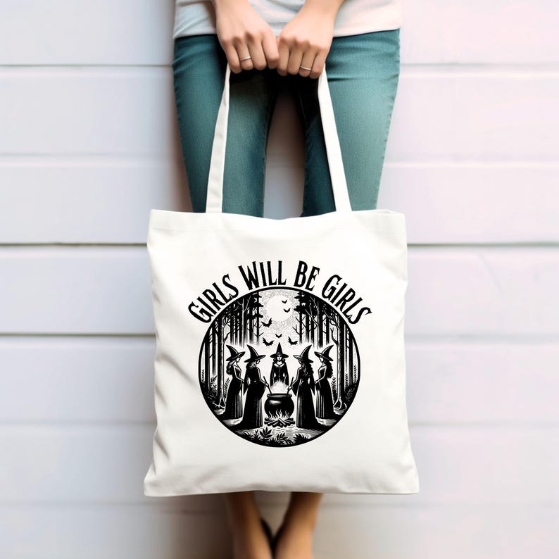 May include: White tote bag with black text and graphic. The text reads "Girls Will Be Girls". The graphic is a circle with a moon, bats, and five witches standing around a cauldron in a forest.