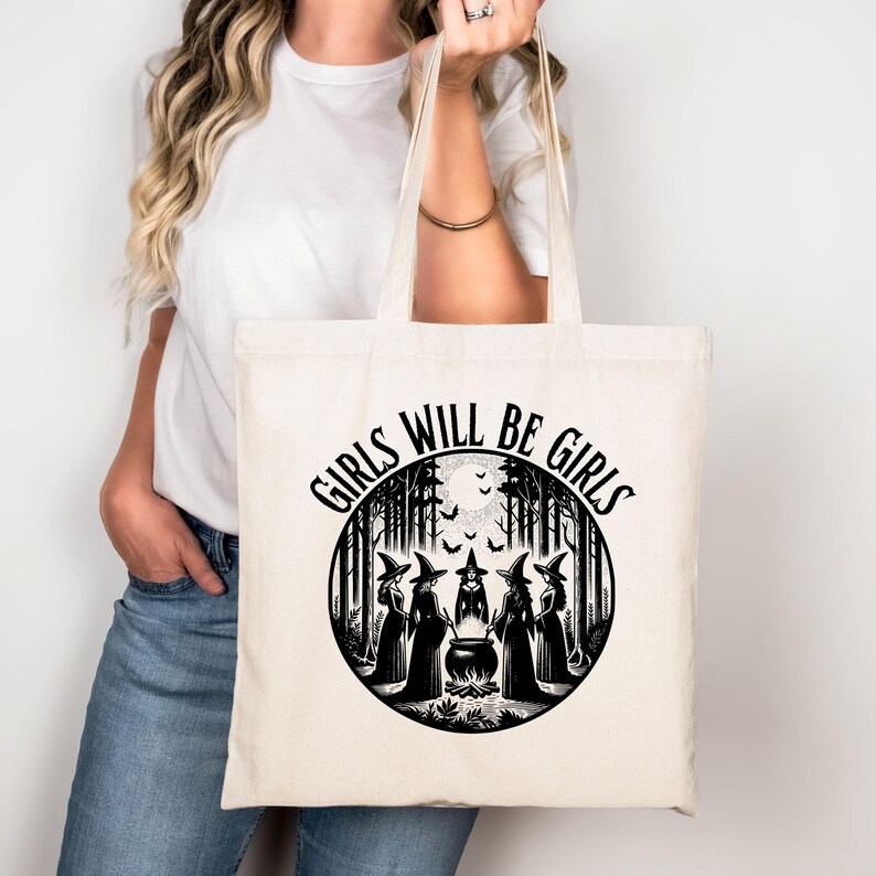 May include: A white tote bag with a black circle design featuring a group of witches in a forest setting. The text "Girls Will Be Girls" is written around the circle.