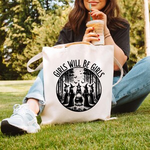 May include: White canvas tote bag with black text that reads "Girls Will Be Girls" and a black and white illustration of five witches in a forest setting around a cauldron.