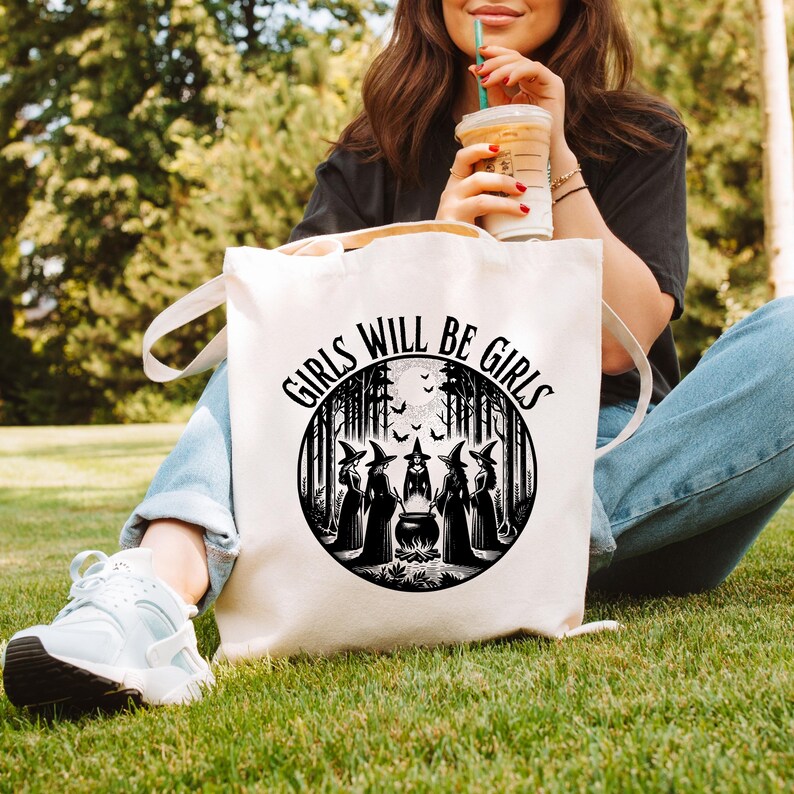 May include: White canvas tote bag with black text that reads "Girls Will Be Girls" and a black and white illustration of five witches in a forest setting around a cauldron.