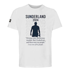 May include: White t-shirt with the text "SUNDERLAND 2024" and a silhouette of a person in the rain. The shirt also features a quote about community. A small black and white logo is on the left sleeve.