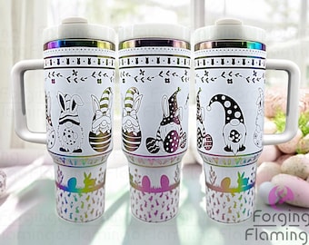 May include: Three white stainless steel travel mugs with a rainbow iridescent finish. Each mug features a different Easter-themed design with gnomes and bunnies. The designs are in black and white.