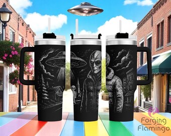 May include: Three black travel mugs with white lids and handles, each featuring a different black and white illustration of an alien and a UFO. The mugs have a straw and are on a colorful surface.