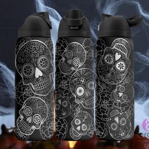 May include: Three black water bottles with silver sugar skull designs. Each bottle features a flip-top lid and a repeating pattern of detailed skulls with floral and geometric elements. The background has a dark, smoky effect.