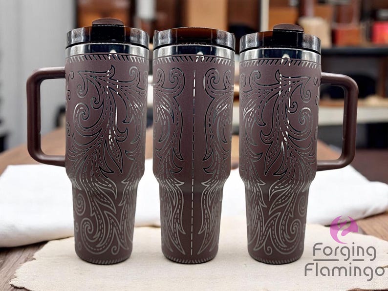 Pode incluir: Tr&ecirc;s canecas de viagem marrons com desenhos florais prateados e al&ccedil;as marrons. As canecas t&ecirc;m uma borda de a&ccedil;o inoxid&aacute;vel e uma tampa marrom escura. As canecas est&atilde;o em uma mesa de madeira.