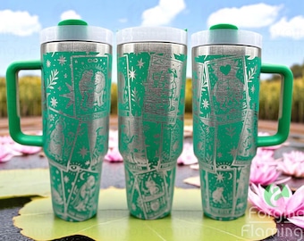 May include: Three green travel mugs with white lids and handles. Each mug features a tarot card design in silver. The mugs are decorated with images of stars, moons, and other tarot symbols. The mugs are sitting on a lily pad.
