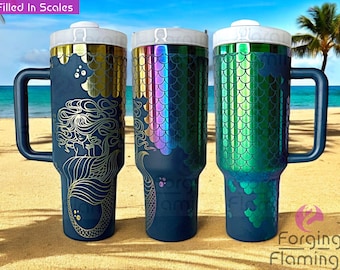 May include: Three stainless steel travel mugs with mermaid scale designs. The mugs are blue with gold, iridescent, and green scales. The mugs have a handle and a lid.