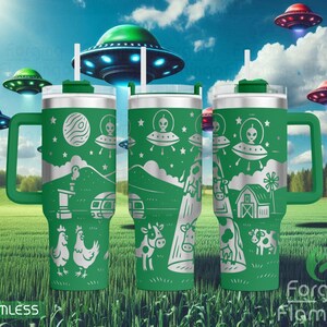 May include: Green travel mug with a handle, featuring a silver alien and spaceship design. The design includes farm animals, mountains, and a barn. The background shows flying saucers and a field. The mug has a white straw and a green lid.