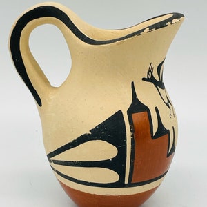 May include: A small, hand-painted ceramic pitcher with a black and white geometric design. The pitcher has a brown base and a black handle.