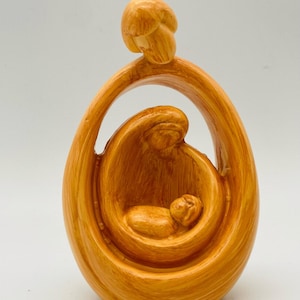 May include: A wooden sculpture of a family, with the mother holding a baby in her arms, and the father standing behind them. The sculpture is painted in a light brown color.