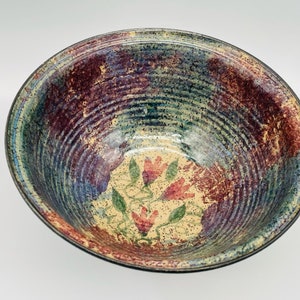 May include: A large, round ceramic bowl with a blue, green, and brown speckled glaze. The bowl has a floral design in shades of pink and green.