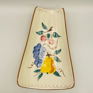 May include: A white ceramic serving dish with a brown rim and a fruit design. The dish features a pear, grapes, and cherries in shades of yellow, blue, green, pink, and red.