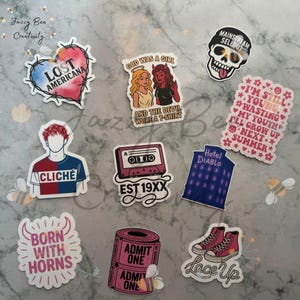 Puede incluir: Una colección de pegatinas coloridas con varios diseños y texto. Las pegatinas incluyen un corazón con "Lost Americana", una calavera, una cinta de cassette con "EST 19XX" y un par de zapatillas altas con "Lace Up". Otras pegatinas presentan frases e ilustraciones.