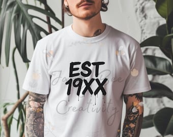 May include: White t-shirt with the text "EST 19XX Creativity" in black. The shirt has a crew neck and short sleeves. The design has a dripping effect. The shirt is worn by a person.