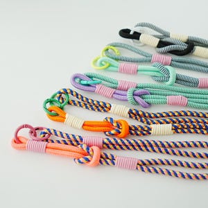 Pode incluir: Uma cole&ccedil;&atilde;o de cinco cord&otilde;es tran&ccedil;ados com v&aacute;rias combina&ccedil;&otilde;es de cores, incluindo laranja, azul, roxo, verde menta e preto. Cada cord&atilde;o inclui um la&ccedil;o com n&oacute;, um anel de metal e amarra&ccedil;&otilde;es de cord&atilde;o em cores contrastantes.