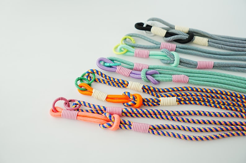 Pode incluir: Uma cole&ccedil;&atilde;o de cinco cord&otilde;es tran&ccedil;ados com v&aacute;rias combina&ccedil;&otilde;es de cores, incluindo laranja, azul, roxo, verde menta e preto. Cada cord&atilde;o inclui um la&ccedil;o com n&oacute;, um anel de metal e amarra&ccedil;&otilde;es de cord&atilde;o em cores contrastantes.