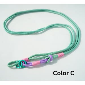 Pode incluir: Um cord&atilde;o longo de corda verde-menta com um padr&atilde;o de tecido texturizado. O cord&atilde;o apresenta uma sec&ccedil;&atilde;o com n&oacute; roxo, duas amarra&ccedil;&otilde;es em rosa brilhante e dois pequenos an&eacute;is circulares azul-petr&oacute;leo na extremidade. O texto Color C &eacute; vis&iacute;vel.
