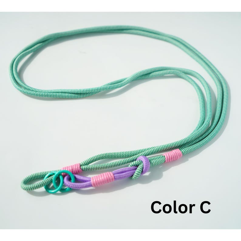 Pode incluir: Um cord&atilde;o longo de corda verde-menta com um padr&atilde;o de tecido texturizado. O cord&atilde;o apresenta uma sec&ccedil;&atilde;o com n&oacute; roxo, duas amarra&ccedil;&otilde;es em rosa brilhante e dois pequenos an&eacute;is circulares azul-petr&oacute;leo na extremidade. O texto Color C &eacute; vis&iacute;vel.