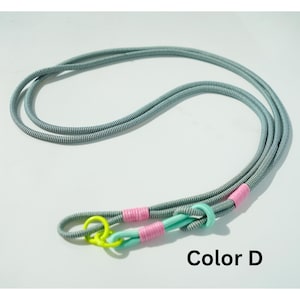 Pode incluir: Uma trela de corda longa com pintas cinzentas e brancas, com um anel amarelo n&eacute;on brilhante, detalhes em verde menta claro e enrolamentos de fio cor-de-rosa vibrante. O texto Color D est&aacute; impresso a preto no canto inferior direito.