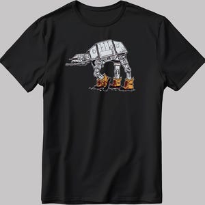 Puede incluir: Camiseta negra con una ilustración humorística de un caminante AT-AT de Star Wars con botas marrones. El diseño es en blanco y gris. La camiseta tiene cuello redondo y es de material suave.