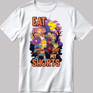 May include: White t-shirt featuring a Halloween-themed graphic with characters from The Simpsons. The design includes the text "EAT MY SHORTS" in orange and black, with Homer Simpson holding a donut. The background features a purple sky and silhouettes of trees.