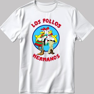 Peut inclure: T-shirt blanc avec un cercle bleu et deux poulets de dessin animé portant des chapeaux et des écharpes. Le texte "Los Pollos Hermanos" est écrit en rouge et noir autour du cercle.