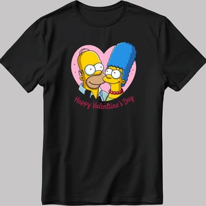 Puede incluir: Una camiseta negra con un diseño de corazón rosa con Homer y Marge Simpson de Los Simpson. El texto "Happy Valentine's Day" está impreso debajo del corazón.