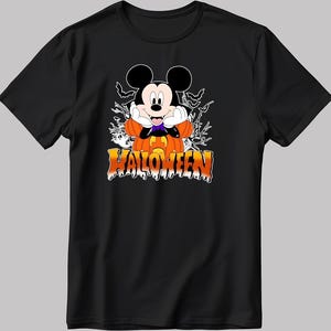 Può includere: T-shirt nera con grafica a tema Halloween. Il design include un personaggio dei cartoni animati con grandi orecchie nere, una zucca e la scritta "HALLOWEEN" in arancione e giallo. Sono inclusi anche pipistrelli e un fantasma.