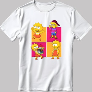 May include: White t-shirt featuring a graphic of four different cartoon images of a yellow-haired girl in a red dress. The girl is shown in various poses, including holding books, wearing glasses, and standing with her hands on her hips. The background of the graphic is a grid of pink and orange squares.