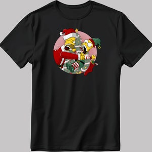 May include: A black t-shirt featuring a circular graphic of a yellow cartoon character dressed as Santa Claus fighting with another yellow cartoon character dressed as an elf. The characters are fighting over a Christmas tree.