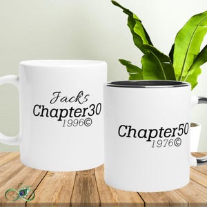 Puede incluir: Dos tazas de café blancas con texto negro. Una taza dice "Jacks Chapter 30 1996©" y la otra "Chapter 50 1976©". Las tazas están sobre una superficie de madera con una planta en el fondo.