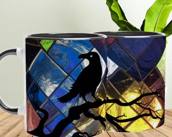May include: Two white ceramic mugs with a black raven perched on a tree branch design. The background features a stained glass pattern in shades of blue, yellow, and green. The mug handles are white with a black interior.