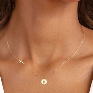 May include: A gold chain necklace with a small cross charm and a round pendant with the letter 'K' on it.