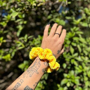 May include: A bright yellow scrunchie made of soft, fluffy fabric. The scrunchie is worn on a person's wrist.