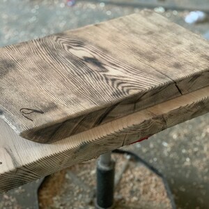 Könnte beinhalten: Zwei Holzschneidebretter, eines auf dem anderen. Das obere Brett ist dunkelbraun und hat eine raue, rustikale Textur. Das untere Brett ist heller und hat eine glattere Oberfläche. Beide Bretter haben ein natürliches Holzmaserungsmuster.