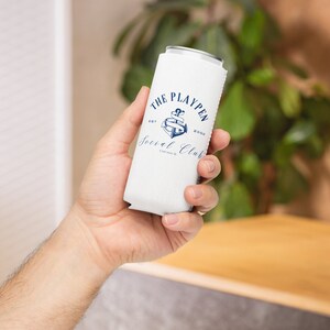 Può includere: Frigorifero per lattine bianco con un design a forma di ancora blu e il testo "The Playpen Social Club Est. 2000" stampato su di esso.