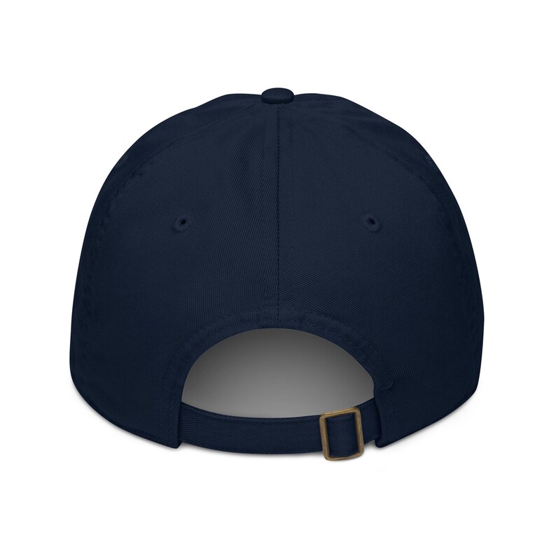 May include: A navy blue baseball cap with a curved brim. The back of the cap features an adjustable strap with a brass-colored metal buckle for a secure fit. The cap is made of a soft, durable fabric.