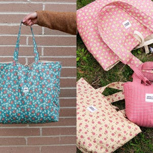 A collection of quilted tote bags in various sizes and patterns. One large teal bag with a floral print is held up. Other bags include pink and cream floral patterns, and a small pink gingham bag. Each bag has a small white label.