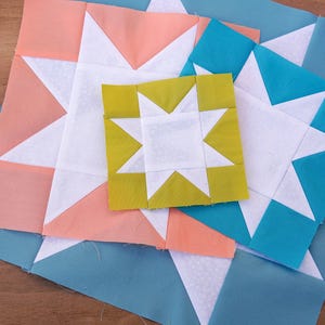 May include: Four fabric squares with a white star design in the center. The squares are layered on top of each other, with the largest square being blue, the next largest being pink, the next being yellow, and the smallest being white.