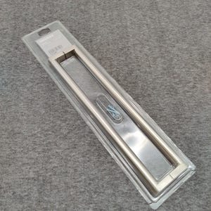 May include: A stainless steel door pull handle in a clear plastic package. The handle is rectangular with a long, flat center section and rounded edges. Screws are included.